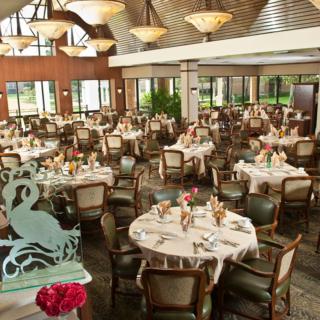 An elegant dining room with neatly arranged tables and chairs, featuring warm decor and intricate chandeliers.