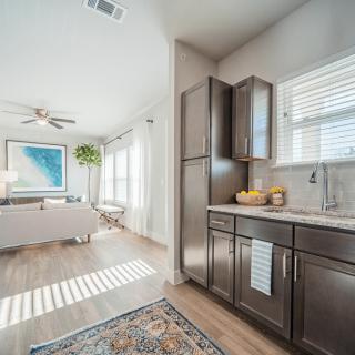 A modern open-concept living area with a kitchen, featuring natural light and wood flooring.