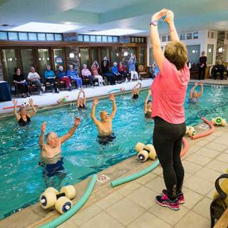 A group of seniors participating in a water exercise class, guided by an instructor on the poolside.
