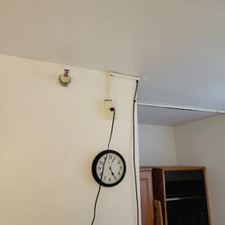 A wall showing a clock, a light fixture, and an exposed cable.