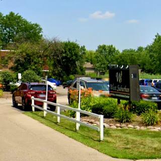 A scenic view of a parking lot with several cars, surrounded by lush greenery and a welcoming sign.