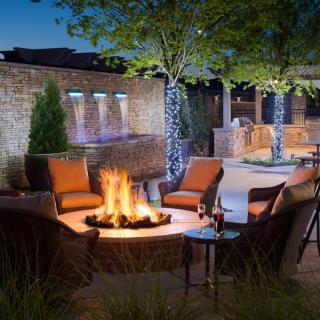 Cozy outdoor patio with a firepit surrounded by comfortable chairs, illuminated by soft evening lights.