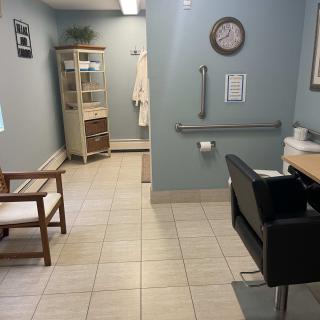 A clean and organized waiting area in a medical office, featuring chairs, shelves, a clock, and tiled flooring.