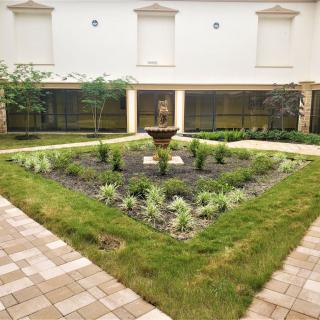 A serene courtyard garden with a central fountain surrounded by greenery and well-maintained landscaping.