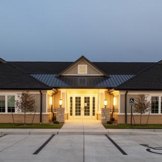 A well-lit building entrance during the evening with an empty parking lot.