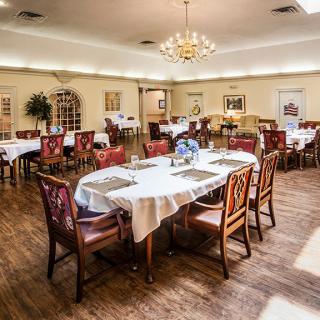 An elegant dining room setup with tables and chairs, featuring a chandelier and wooden flooring.