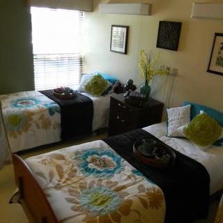 A cozy bedroom with twin beds featuring floral bedding and decorative pillows, illuminated by natural light.