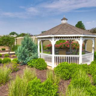 A charming white gazebo surrounded by lush greenery in a landscaped garden under a clear blue sky.