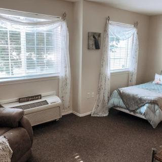 A cozy bedroom with a bed, chair, and large windows draped with curtains.