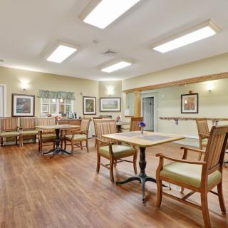 A spacious dining area with wooden flooring and neatly arranged tables and chairs.