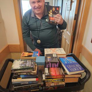 A person standing with a cart full of books indoors.