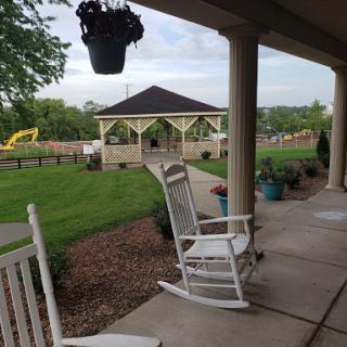 A peaceful outdoor setting featuring rocking chairs on a porch, overlooking a gazebo and lush green lawn.