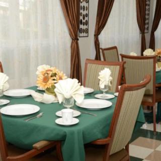 An elegantly set dining table with green tablecloth, surrounded by chairs and decorated with flowers.