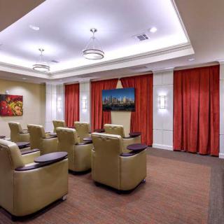 A cozy theater room with comfortable armchairs arranged in front of a large TV, surrounded by elegant red curtains and soft lighting.