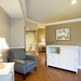 A cozy living room with a blue armchair, white cabinet, and decorative lamp.
