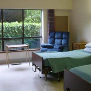A hospital room with two beds, a window, and a chair.
