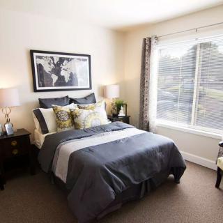 A cozy bedroom with a neatly made bed, large window, lamps on side tables, and artwork on the wall.