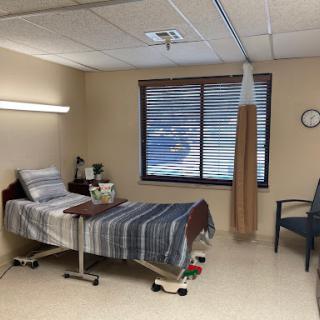 A view of a hospital patient room featuring a bed, chair, and natural light from the window.