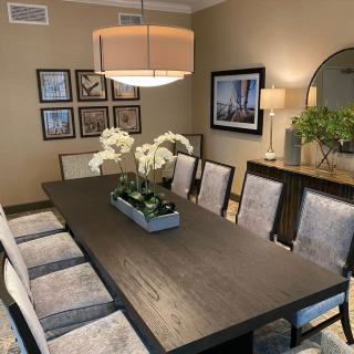 A stylish dining room with a large dark wooden table, surrounded by cushioned chairs and decorated with flowers and artwork.