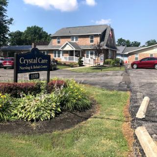 A view of the Crystal Care residential building surrounded by greenery and parked cars.