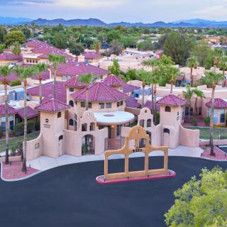 Aerial view of a gated residential community with distinctive architecture and palm trees, set against a backdrop of mountains.