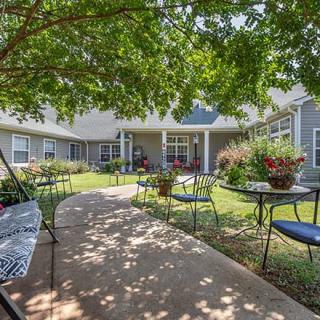 A tranquil garden patio with tables and chairs under the shade of lush trees.