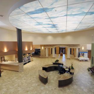 A spacious lobby with a stylish ceiling design resembling a sky, featuring modern reception desks and warm lighting.