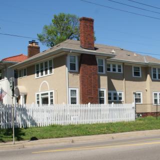 A two-story residential house with a white picket fence and prominent chimneys.