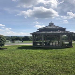 A wooden gazebo stands on a lush green lawn under a partly cloudy sky.