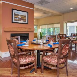 A cozy dining area with elegantly set tables, featuring a warm fireplace and artistic decor.