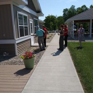 A group of people standing on a sidewalk next to a building and garden on a sunny day.