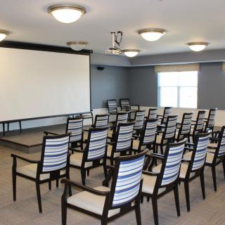 A conference room set up with rows of chairs facing a large screen, ready for a presentation.