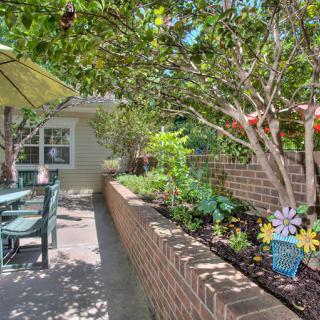 A serene garden patio with outdoor furniture surrounded by lush greenery and a brick wall.