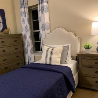 A cozy bedroom with a single bed, adorned with blue and white bedding, a nightstand with a lamp, and matching dressers.