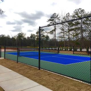 An outdoor tennis court surrounded by a fence, set against a backdrop of trees.