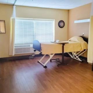 An empty hospital room with a single adjustable bed and wooden flooring.
