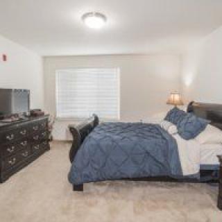A cozy bedroom with a neatly made bed, dresser, lamp, and television.