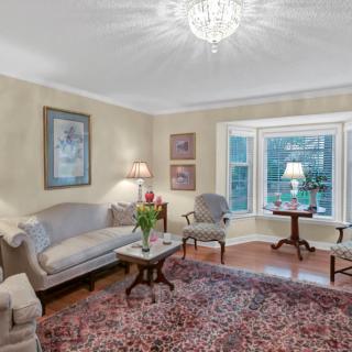 A cozy living room with traditional decor, featuring a chandelier, upholstered seating, and a large window.