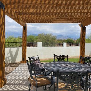 A serene outdoor patio setting under a wooden pergola, complete with a stylish table and chairs, perfect for dining or relaxation.