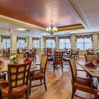 A well-decorated dining room with neatly arranged tables and chairs, featuring elegant lighting and large windows.