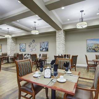 A formal dining area with neatly arranged tables and chairs, decorated with artwork and elegant lighting.