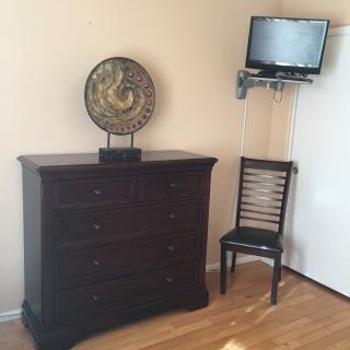 A room with a dark wooden dresser, a decorative clock, a chair, and a wall-mounted TV.