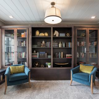 A cozy reading nook featuring a large bookshelf filled with books, two blue armchairs with green pillows, and elegant home decor.