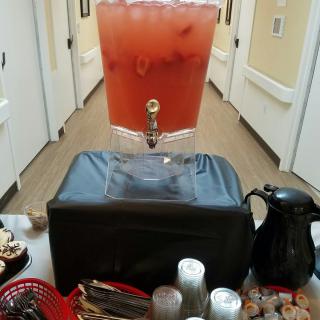 A drink dispenser filled with a red beverage is set up in a hallway, accompanied by snacks and condiments.