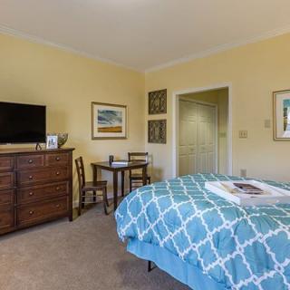 A cozy bedroom featuring a bed with a patterned blue comforter, a wooden dresser with a TV, and various wall decorations.