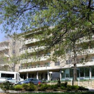 A hospital building surrounded by trees with vehicles parked outside.