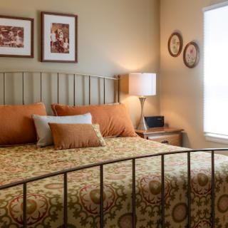 A cozy bedroom featuring a decorative bed with warm-colored bedding, complemented by stylish lamps and framed pictures on the walls.