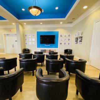 A modern lounge area with comfortable chairs facing a television, featuring a blue accent ceiling.