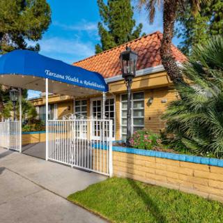 A welcoming entrance to a charming residential building, featuring a blue canopy and lush landscaping.