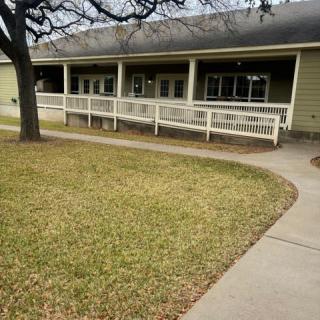 A single-story building with a ramp leading to the entrance, surrounded by grass and a tree.